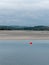 View of Clonakilty Bay at low tide. A small orange buoy is kept on a calm water surface. The sandy shore of the sea bay. The