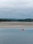 View of Clonakilty Bay at low tide. A small orange buoy is kept on a calm water surface. The sandy shore of the sea bay. The