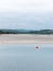 View of Clonakilty Bay at low tide. A small orange buoy is kept on a calm water surface. The sandy shore of the sea bay