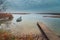 view from the coast of the lake to a beautiful water landscape with a boat, wooden pier and coastal reeds in the light of autumnal