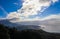 View of the coast and the mountains and a very blue sky with clouds and a vapor trail and the sun highlighting the edge of the oce