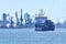 View of commercial cargo port with container bridge cranes and a ship entering port on a sunny day.