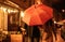 View of couple in autumn outfit walking under umbrella along evening street
