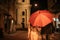 View of couple in autumn outfit walking under umbrella along evening street