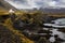 A view of the craggy coastline of Arnarstapi with a solitary house. Autumn colours with snow covered mountains in the background