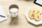 View of a cup of milk and simple colorful biscuits, next to a ebook on a notebook.