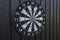 View of dartboard with missiles on black wooden wall isolated.