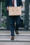 View of dismissed businessman walking on stairs near building and holding box