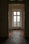 View through the doorway in an empty old villa with wooden parquet floor to a lattice window from dark to bright