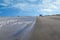 View down a deserted long wet beach with many small birds feeding on the wet sand. There is a dramatic sky