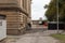 View down the side alley of an abandoned industrial building with unpaved drive and dumpsters