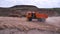 View of driving dump truck on sandy soil. Scene. Orange dump truck rides on quarry with ground in lowlands