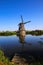 View on dutch water canal with reflection of one old windmill against deep blue cloudless summer sky in rural countryside -