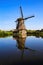 View on dutch water canal with reflection of one old windmill against deep blue cloudless summer sky in rural countryside -