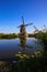 View on dutch water canal with reflection of one old windmill against deep blue cloudless summer sky in rural countryside -