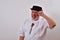 View of an elderly man in a hat scratching his head trying to remember on a white background