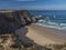 View of empty Praia da Amalia beach with ocean waves, cliffs and stones, wet golden sand and green vegetation at wild