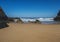 View of empty Praia do Cavaleiro beach with steep rock cliff, ocean waves, stones and wet golden sand at wild Rota