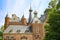 View on facade of medieval dutch fairy castle with towers and clock from 14th century, green trees against blue summer sky -