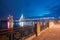 View Of Famous Vansu Cable-Stayed Bridge In Bright Night Illumination From The Deserted Embankment Of The Daugava