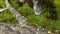 View of feet, legs of a hunter or hiker in rubber boots walking throuhg a swamp and stepping on moss and water