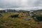 view of field with green grass and scattered stones against small rural houses, Norway, Hardangervidda