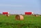 View of a field with hay in rolls against the background of trucks with semi-trailer driving along the highway. Harvesting dry