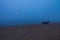 A view of a fisher boat on the beach during an unusual summer foggy morning. Moon, shore and sky