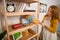 View of foxy woman using whisk to clean shelves from dust.