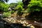 View of fresh river stream, stone bank and natural rock beach with green trees and local buildings in Kurokawa onsen town