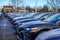 View of the fronts of a row of various colored new cars in a parking lot.