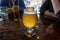 View of a frothy, ice cold farmhouse ale on a wooden table inside a restaurant