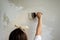 View of a girl from the back who is holding a spatula white putty on a gray gypsum board