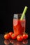 View of glass with Bloody Mary cocktail with celery, on wet slate with cherry tomatoes, black background, vertical