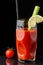 View of glass of Bloody Mary cocktail with lime, celery and straw, on wet slate with cherry tomato, on black background in vertica