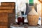 View of a glass bottle and a traditional wooden woven bottle holding several liters. Two empty glasses on the barrel. Small local