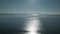 View of glistening and shimmering sea surface with hills on the horizon. Defocused glow of sun reflecting off sea water