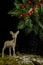 View of golden Christmas deer on moss with snow falling, black background with green leaves and holly,
