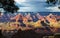 A View of Grand Canyon with rock formations highlighted by the sun on an overcast day framed by trees in the foreground