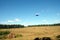 View from the ground to the drone in flight above mowed field with many rolled haystacks under blue sky with light white clouds in