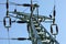 View from ground to power pylon top. Cables and ceramic isolators visible against blue sky. Abstract power industry background