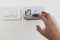 View of a hand adjusting the heating temperature. Digital thermostat on the wall of the house