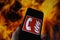 View on hand holding mobile phone with international fire emergency telephone symbol. Blurred fire flames background. Selective