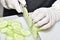 View of hands with gloves slicing a peeled cucumber with a kitchen knife on a cutting board