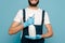 View of happy cleaner in uniform and rubber gloves holding spray detergent on blue background