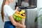 View of happy girl opening fridge and holding groceries