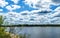 View from the high bank to the wide river. Riverbank with forest under the clouds