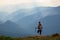 The view with the high mountains in fog. The sun rays are enlighten the forests. The extreme girl with the tracking sticks.