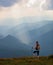 The view with the high mountains in fog. The sun rays are enlighten the forests. The extreme girl with the tracking sticks.