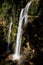 View of a high waterfall with sunlight and surrounded by rainforest